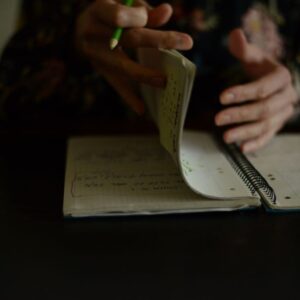 a woman writing in a notebook with a green pencil